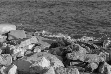 Siyah ve beyaz okyanus dalgaları kıyıdaki kayalara sıçrar ve hava köpüğü oluşturur.