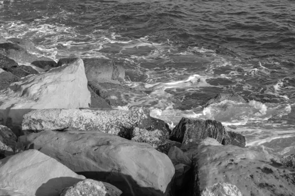 Siyah ve beyaz okyanus dalgaları kıyıdaki kayalara sıçrar ve hava köpüğü oluşturur.