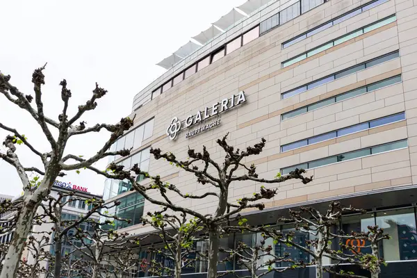 Frankfurt, Almanya - 18 Nisan 2025: Frankfurt şehir merkezindeki büyük bir mağaza olan Hauptwache 'deki GALERIA' nın dış görünümü, bulutsuz bir yay gökyüzü altında yapraksız uçak ağaçları tarafından çerçevelenmiştir.