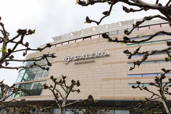 Frankfurt, Almanya - 18 Nisan 2025: Frankfurt şehir merkezindeki büyük bir mağaza olan Hauptwache 'deki GALERIA' nın dış görünümü, bulutsuz bir yay gökyüzü altında yapraksız uçak ağaçları tarafından çerçevelenmiştir.