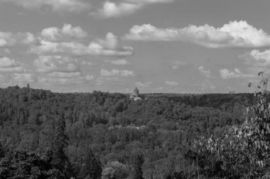 Sigulda, Letonya - 21 Temmuz 2025: Turaida Catle Müzesi, orman yemyeşil ağaçları arasındaki uzaklıktan siyah ve beyaz