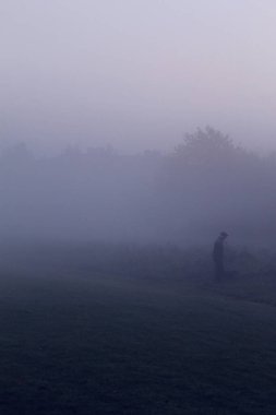 Sabahın erken saatlerinde köpeği gezdiren yaşlı bir adam. Sis ve sis