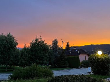 Ağaçlarla ve dağlarla çevrili bir yerde turuncu ve pembe gün batımı