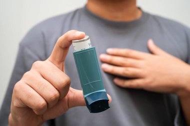 Astım ve kronik obstrüktif akciğer hastalığı COPD, Asyalı genç adam ölçülü doz solunum cihazı kullanıyor..