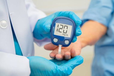Diyabet tedavisinde kan şekeri seviyesini kontrol etmek için dijital glikoz ölçer kullanan Asyalı doktor.