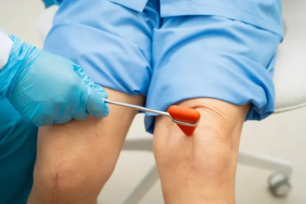Asyalı doktor, hastanedeki yaşlı hastayı muayene etmek için diz refleksi sinirine vurdu..
