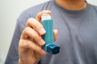 Astım ve kronik obstrüktif akciğer hastalığı COPD, Asyalı genç adam ölçülü doz solunum cihazı kullanıyor..