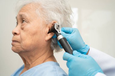 Otolaryngologist ya da ENT hekim doktoru yaşlı hasta kulağını otoskopla muayene ediyor, işitme sorunu var..