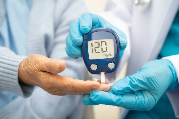 Diyabet tedavisinde kan şekeri seviyesini kontrol etmek için dijital glikoz ölçer kullanan Asyalı doktor.