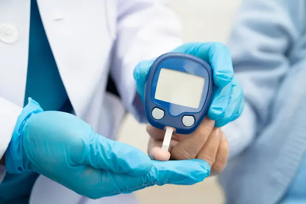 Diyabet tedavisinde kan şekeri seviyesini kontrol etmek için dijital glikoz ölçer kullanan Asyalı doktor.
