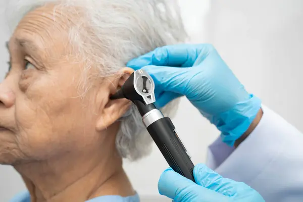 Otolaryngologist ya da ENT hekim doktoru yaşlı hasta kulağını otoskopla muayene ediyor, işitme sorunu var..