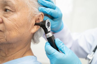 Otolaryngologist ya da ENT hekim doktoru yaşlı hasta kulağını otoskopla muayene ediyor, işitme sorunu var..