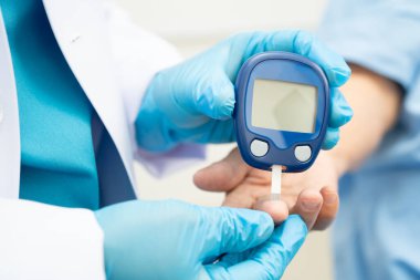 Diyabet tedavisinde kan şekeri seviyesini kontrol etmek için dijital glikoz ölçer kullanan Asyalı doktor.