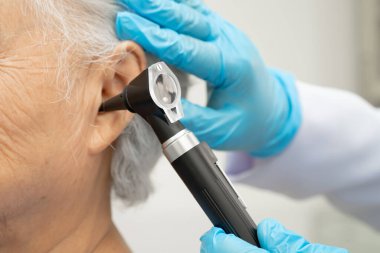 Otolaryngologist ya da ENT hekim doktoru yaşlı hasta kulağını otoskopla muayene ediyor, işitme sorunu var..