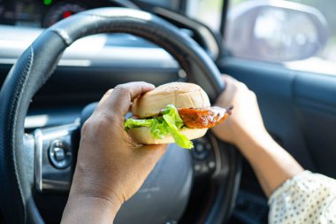 Asyalı kadın sürücü arabada hamburger yiyip, tutar, tehlikeli ve kaza riskini göze alır..