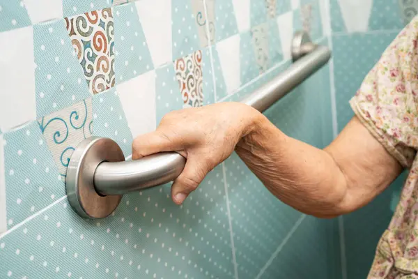 Asyalı yaşlı kadın hasta tuvaletteki destek parmaklıklarında tırabzan emniyeti kullanıyor..