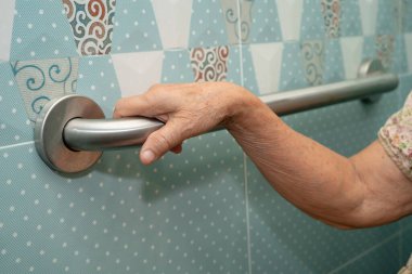 Asyalı yaşlı kadın hasta tuvaletteki destek parmaklıklarında tırabzan emniyeti kullanıyor..