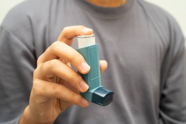 Astım ve kronik obstrüktif akciğer hastalığı COPD, Asyalı genç adam ölçülü doz solunum cihazı kullanıyor..