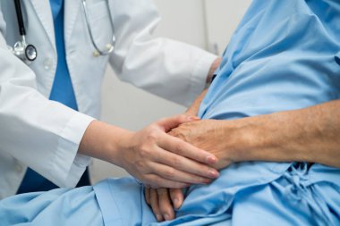Asyalı doktor yaşlı kadın hasta sağlığını hastanede kontrol edip tedavi ediyor.