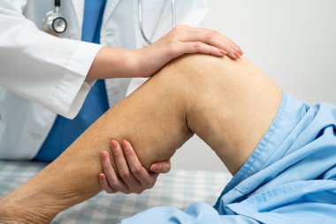 Doktor, hastanede dizinde yara izi olan Asyalı yaşlı kadın hastayı kontrol ediyor..