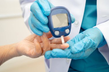 Diyabet tedavisinde kan şekeri seviyesini kontrol etmek için dijital glikoz ölçer kullanan Asyalı doktor.