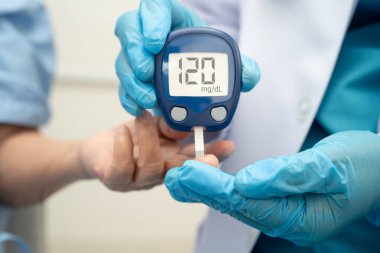 Diyabet tedavisinde kan şekeri seviyesini kontrol etmek için dijital glikoz ölçer kullanan Asyalı doktor.