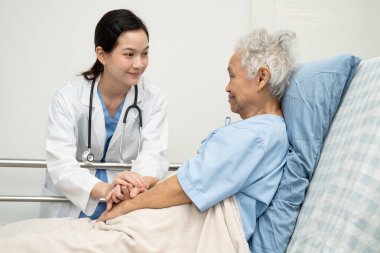 Asyalı doktor yaşlı kadın hasta sağlığını hastanede kontrol edip tedavi ediyor.