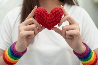 Asyalı LGBT kadını elinde kalp gökkuşağı bayrağı tutuyor.