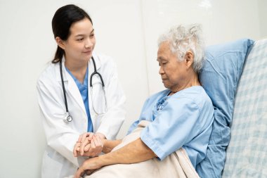 Asyalı doktor yaşlı kadın hasta sağlığını hastanede kontrol edip tedavi ediyor.