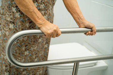 Asyalı yaşlı kadın hasta tuvalette tuvalet desteği kullanıyor..
