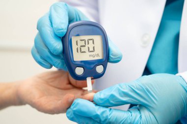 Diyabet tedavisinde kan şekeri seviyesini kontrol etmek için dijital glikoz ölçer kullanan Asyalı doktor.