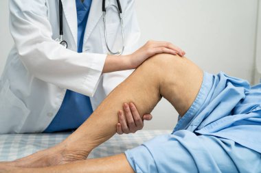 Doktor, hastanede dizinde yara izi olan Asyalı yaşlı kadın hastayı kontrol ediyor..