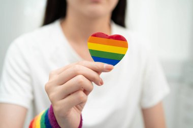 Asyalı LGBT kadını elinde kalp gökkuşağı bayrağı tutuyor.