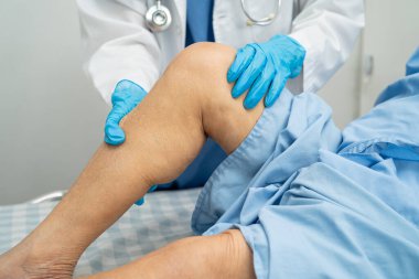 Doktor, hastanede dizinde yara izi olan Asyalı yaşlı kadın hastayı kontrol ediyor..