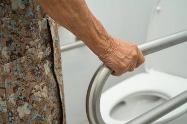 Asyalı yaşlı kadın hasta tuvalette tuvalet desteği kullanıyor..