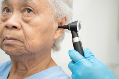 Otolaryngologist ya da ENT hekim doktoru yaşlı hasta kulağını otoskopla muayene ediyor, işitme sorunu var..