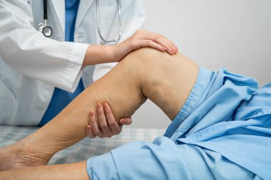 Doktor, hastanede dizinde yara izi olan Asyalı yaşlı kadın hastayı kontrol ediyor..