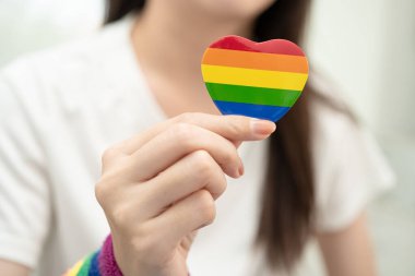 Asyalı LGBT kadını elinde kalp gökkuşağı bayrağı tutuyor.