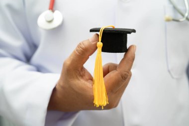 Hastanede mezun şapkası tutan Asyalı kadın doktor. Tıp eğitimi almış..