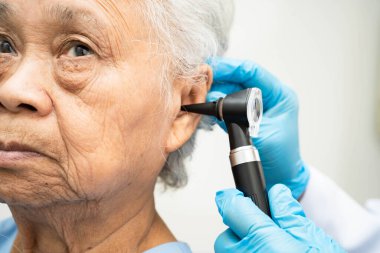 Otolaryngologist ya da ENT hekim doktoru yaşlı hasta kulağını otoskopla muayene ediyor, işitme sorunu var..
