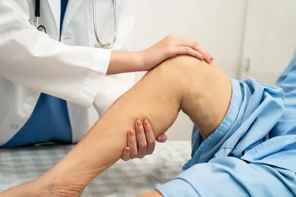 Doktor, hastanede dizinde yara izi olan Asyalı yaşlı kadın hastayı kontrol ediyor..