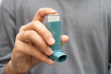 Astım ve kronik obstrüktif akciğer hastalığı COPD, Asyalı genç adam ölçülü doz solunum cihazı kullanıyor..