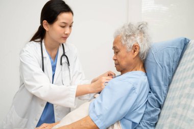 Asyalı doktor yaşlı kadın hasta sağlığını hastanede kontrol edip tedavi ediyor.