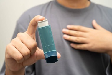 Astım ve kronik obstrüktif akciğer hastalığı COPD, Asyalı genç adam ölçülü doz solunum cihazı kullanıyor..