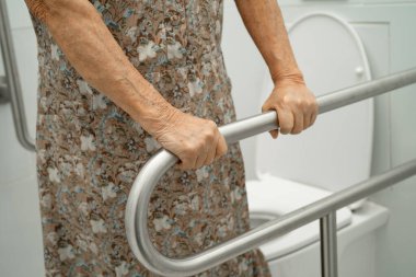 Asyalı yaşlı kadın hasta tuvalette tuvalet desteği kullanıyor..