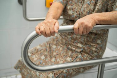 Asyalı yaşlı kadın hasta tuvalette tuvalet desteği kullanıyor..