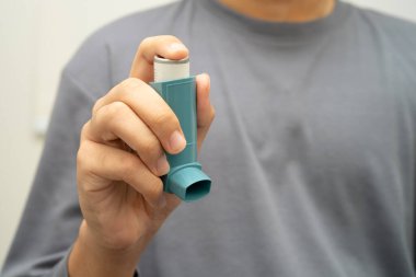 Astım ve kronik obstrüktif akciğer hastalığı COPD, Asyalı genç adam ölçülü doz solunum cihazı kullanıyor..