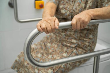 Asyalı yaşlı kadın hasta tuvaletteki destek parmaklıklarında tırabzan emniyeti kullanıyor..