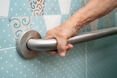 Asyalı yaşlı kadın hasta tuvaletteki destek parmaklıklarında tırabzan emniyeti kullanıyor..