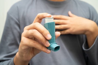 Astım ve kronik obstrüktif akciğer hastalığı COPD, Asyalı genç adam ölçülü doz solunum cihazı kullanıyor..